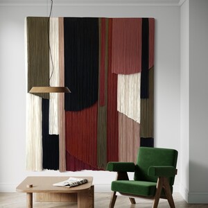 May include: A green velvet armchair with wooden legs sits in front of a large wall hanging made of colorful yarn strands. A wooden coffee table with a magazine on top sits in front of the chair.