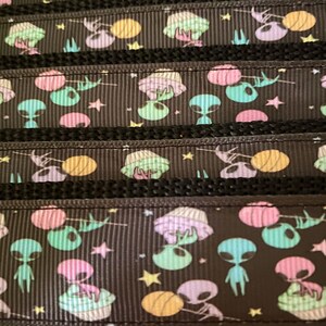 K&ouml;nnte beinhalten: Schwarzes Band mit einem sich wiederholenden Muster aus pastellfarbenen Au&szlig;erirdischen, UFOs, Sternen und Planeten. Das Band hat ein strukturiertes, geripptes Aussehen mit einem schwarzen Rand. Die Au&szlig;erirdischen sind in Gr&uuml;n-, Lila- und Blaut&ouml;nen gehalten.
