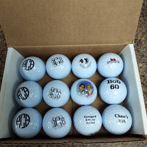 May include: A dozen personalized golf balls in a cardboard box. Each ball features custom designs, including initials, a photo, and text such as "Bob 60", "Grandpa B is by par the best", and "Chase's 35th".