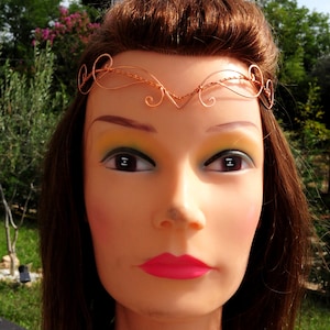 May include: A copper wire headband with a delicate, swirling design. The headband is worn on a mannequin with long brown hair and pink lipstick.