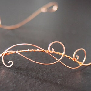 May include: A delicate copper wire headband with a swirling design. The headband is made of thin wire and has a simple, elegant look.