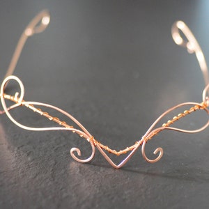May include: A delicate copper wire headband with a swirling design. The headband is made of thin wire and has a delicate, feminine look.