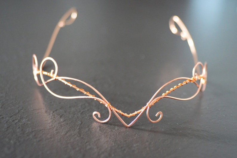 May include: A delicate copper wire headband with a swirling design. The headband is made of thin wire and has a delicate, feminine look.