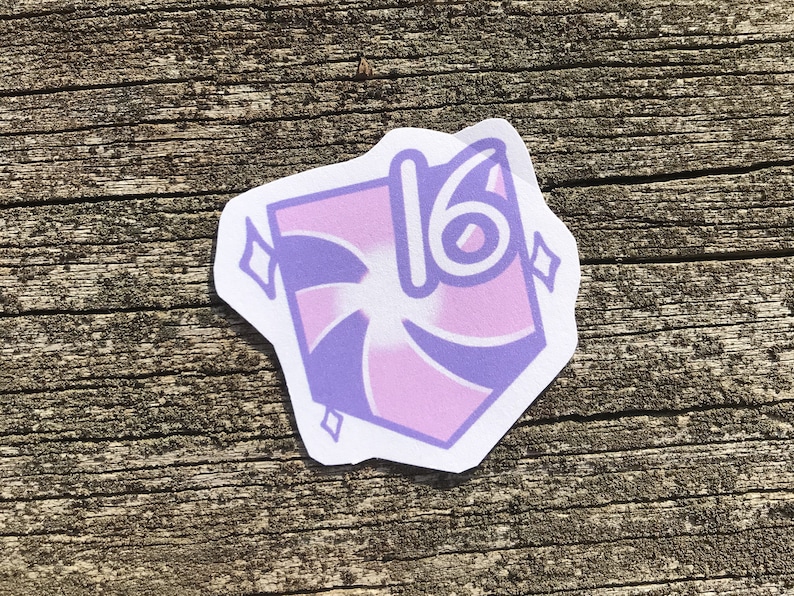 May include: A pink and purple sticker with a swirl design and the number 16 in the centre. The sticker has a white border and is on a wooden surface.