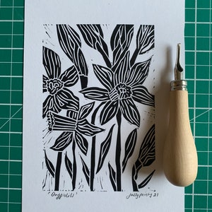 Op de afbeelding: Zwart-witte linosnede van narcissen met de tekst "Daffodils" en "Jazzy Prints 21" in de onderste hoeken.