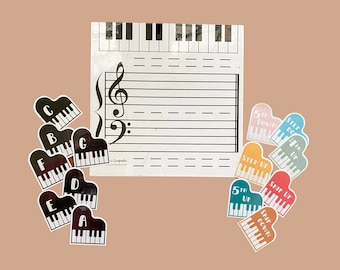 May include: Educational music learning set featuring a white sheet music template with a treble and bass clef, piano keyboard, and colorful piano-shaped stickers labeled with musical notes and terms like "Step Up" and "5th Down".
