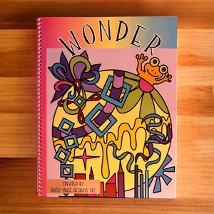 May include: A colorful spiral bound coloring book with the word "WONDER" in large letters on the cover. The cover features a yellow, green, and purple abstract design with a frog on top. The book is titled "WONDER" and says "CREATED BY DAISY MUSE DESIGNS, LLC" at the bottom.