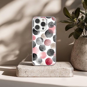 May include: Clear phone case with a watercolor pattern of pink, gray, black, and tan circles on a white background. The case is displayed on a small, textured, rectangular stone block.