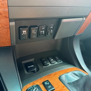 May include: Interior car console with various buttons and switches. Features include controls for VSC, auxiliary lights, heated seats, and a 12V/120W power outlet. The console has a wood grain finish and a control dial for comfort and sport settings.