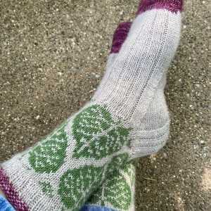 Puede incluir: Un par de calcetines de punto con un patrón de hojas verdes y blancas. Los calcetines tienen un puño burdeos.
