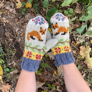 May include: A pair of grey knitted mittens with a fox design. The mittens have a blue, yellow and red trim.