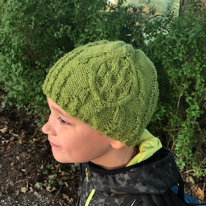 Puede incluir: Un gorro de punto verde con un patrón de trenza. El gorro lo lleva puesto un niño.