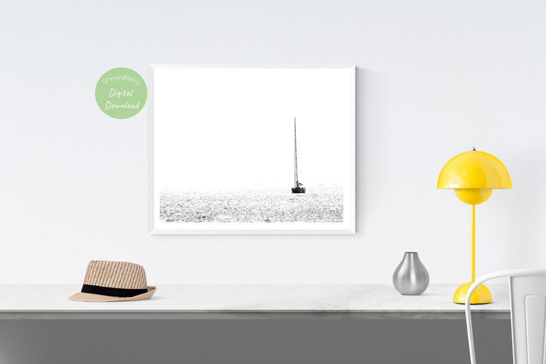 K&ouml;nnte beinhalten: Schwarz-Wei&szlig;-Druck eines Segelboots auf dem Wasser. Das Kunstwerk ist minimalistisch, mit dem Boot und seinem Mast in der Mitte vor einem hellen Hintergrund. Das Bild ist ein digitaler Download.