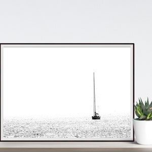 K&ouml;nnte beinhalten: Schwarz-Wei&szlig;-Druck eines Segelboots auf dem Wasser. Das Kunstwerk ist minimalistisch, mit dem Boot und seinem Mast als Silhouette vor einem hellen, strukturierten Meer. Rechts befindet sich eine kleine Sukkulente in einem wei&szlig;en Topf.