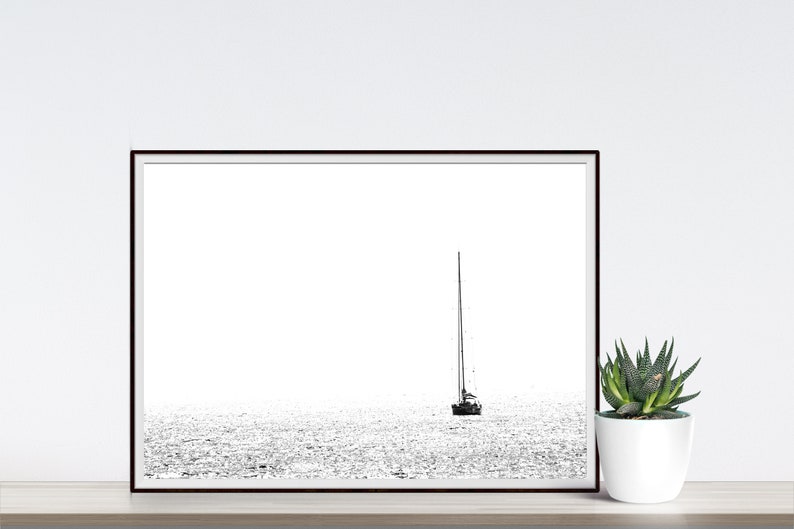 K&ouml;nnte beinhalten: Schwarz-Wei&szlig;-Druck eines Segelboots auf dem Wasser. Das Kunstwerk ist minimalistisch, mit dem Boot und seinem Mast als Silhouette vor einem hellen, strukturierten Meer. Rechts befindet sich eine kleine Sukkulente in einem wei&szlig;en Topf.