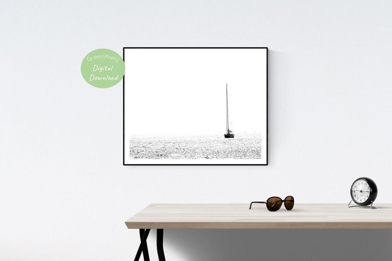 K&ouml;nnte beinhalten: Schwarz-Wei&szlig;-Druck eines Segelboots auf dem Wasser in einem Rahmen. Das minimalistische Bild zeigt ein Segelboot mit hohem Mast auf einer Wasserfl&auml;che. Der Druck ist an einer wei&szlig;en Wand angebracht und hat einen schwarzen Rahmen.