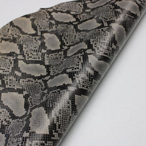 Puede incluir: Primer plano de un trozo de cuero de serpiente gris y negro. El cuero tiene una superficie texturizada y está doblado por la mitad.