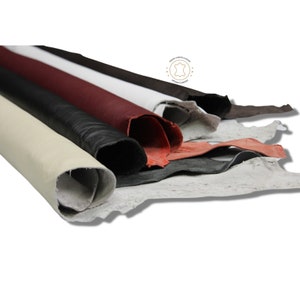 May include: A variety of leather hides in different colors, including white, black, red, and brown. The hides are rolled up and arranged in a pile.