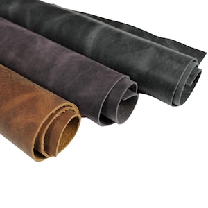 Peut inclure: Trois rouleaux de cuir de différentes couleurs : marron, violet et gris. Le cuir est enroulé et les bords sont visibles.