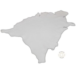 May include: A white leather hide with a slightly irregular shape. The hide is smooth and appears to be soft. A small, circular logo with the text "PREMIUM TANNED LEATHER" and "ITALIAN COMPANY" is visible in the lower right corner.