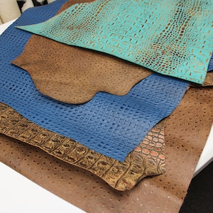 May include: A stack of different colored leather pieces with embossed crocodile and ostrich patterns. The leather is brown, blue, and turquoise.