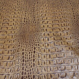 以下が含まれることがあります： 茶色のワニ革の質感のクローズアップ。革は、隆起した鱗模様と微妙な光沢があります。