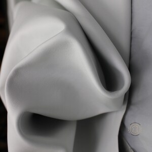 May include: Close-up of a smooth, light gray leather hide. The leather is folded and draped, showing its texture and flexibility.