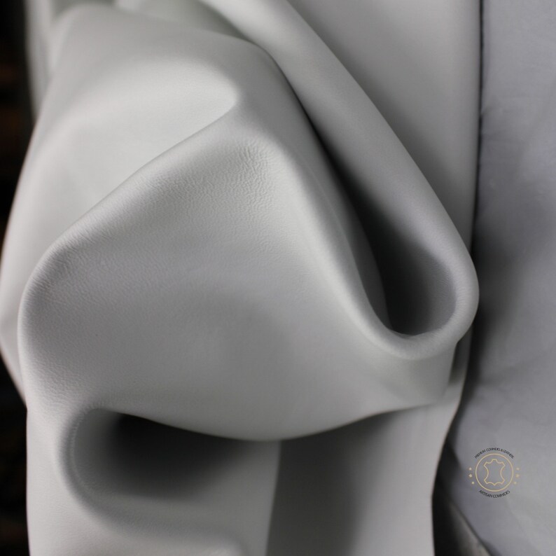 May include: Close-up of a smooth, light gray leather hide. The leather is folded and draped, showing its texture and flexibility.