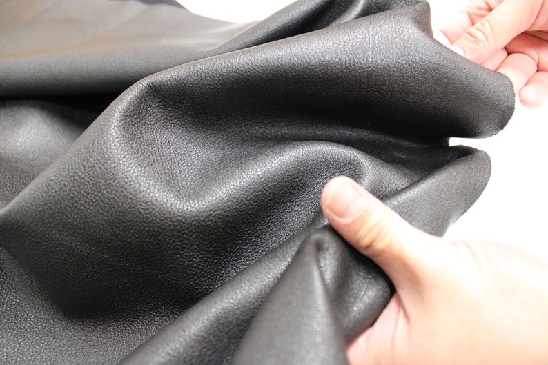 K&ouml;nnte beinhalten: Nahaufnahme von schwarzem Leder mit einer genarbten Textur. Das Leder ist weich und geschmeidig und wird von einer Hand gehalten.