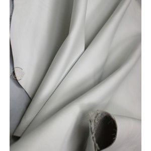 May include: Close-up of a smooth, light gray leather fabric. The fabric is folded and draped, showing its texture and drape.