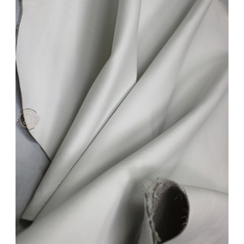 May include: Close-up of a smooth, light gray leather fabric. The fabric is folded and draped, showing its texture and drape.