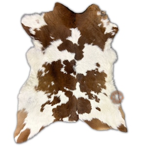 Puede incluir: Alfombra de piel de vaca marrón y blanca con un patrón natural de manchas. La piel es suave y esponjosa, y los colores son ricos y vibrantes.
