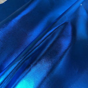 May include: A close-up of a vibrant blue metallic fabric with a smooth, shiny surface. The fabric is folded in half, revealing the texture and sheen.