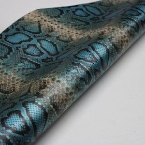 Op de afbeelding: Blauw en bruin geweven stof met een slangenhuidpatroon en een glanzende afwerking.
