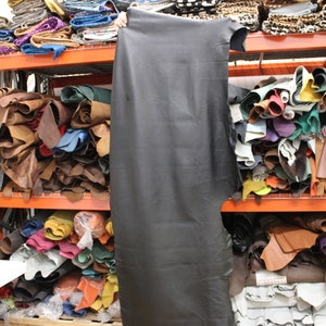 K&ouml;nnte beinhalten: Ein gro&szlig;es Regal gef&uuml;llt mit Lederrollen in verschiedenen Farben, darunter Braun, Beige, Schwarz, Gr&uuml;n und Blau. Das Leder ist gestapelt und gerollt, und einige St&uuml;cke h&auml;ngen an den Regalen.