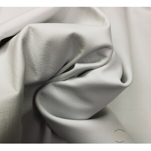 May include: Close-up of a smooth, light gray leather fabric. The fabric is folded and draped, showing its texture and drape.