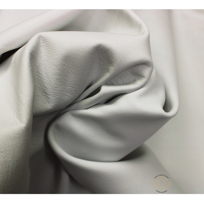 May include: Close-up of a smooth, light gray leather fabric. The fabric is folded and draped, showing its texture and drape.