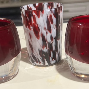 Könnte beinhalten: Drei dekorative Gläser. Zwei sind oben tiefrot mit einem klaren Boden. Das dritte ist ein hohes Glas mit einem weiß-roten Sprenkelmuster. Diese Gläser sind für Getränke geeignet.