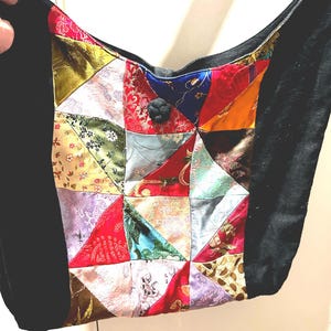 May include: A shoulder bag featuring a patchwork design of various colorful satin fabrics with floral and geometric patterns. The bag has solid black side panels and a central black knot button closure at the top opening of the main compartment.