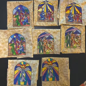 May include: A collection of eight fabric squares, each featuring a stained-glass style design. The designs depict religious scenes with figures in colorful robes, set against a beige background. The images include angels and biblical figures.