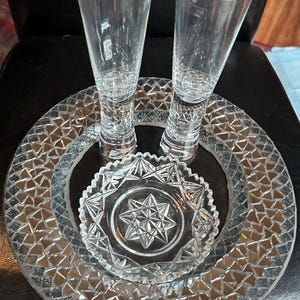 May include: Clear glass stemware set, including two tall, slender glasses and a decorative plate arrangement. The plates feature a geometric pattern and a star-shaped design in the center. The set is ideal for serving beverages.