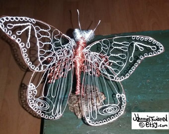 May include: A wire sculpture of a butterfly with copper and silver wire. The butterfly's wings are detailed with intricate patterns and the body is made of copper wire.