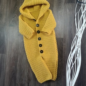 May include: A mustard yellow crocheted baby onesie with a hood and button closure.