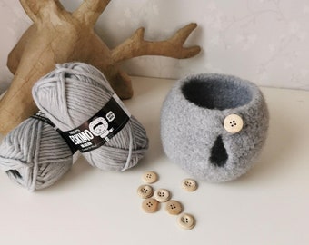 May include: Two balls of gray yarn with a black label that says "Eskimo" and a cartoon image of a person wearing a hat. There are also several wooden buttons scattered on a white surface.