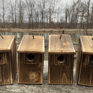 May include: Four rustic wooden birdhouses with dark brown stain and a natural wood finish. Each birdhouse has a small, round entrance hole and a slanted roof.