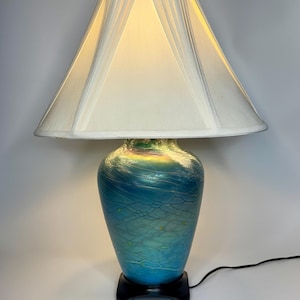 May include: A blue and green glass table lamp with a white lampshade. The lamp has a swirl design and a black base.