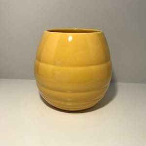 May include: A yellow ceramic vase with a ribbed design. The vase is round and has a smooth, glossy finish.