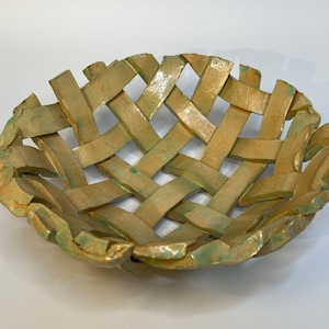 May include: A woven ceramic bowl with a green glaze. The bowl is made of individual strips of clay that are woven together to create a basket-like design.