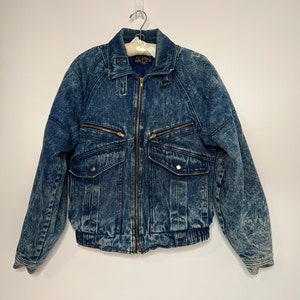 Puede incluir: Una chaqueta vaquera azul con cierre de cremallera y varios bolsillos. La chaqueta tiene un aspecto descolorido, lavado con ácido.