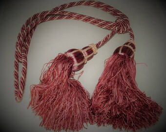 May include: A pair of burgundy tassel tiebacks with a cream and burgundy striped cord. The tassels are made of a soft, fluffy material.